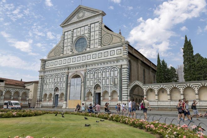 The striking front view of Santa Maria Novella Church in Florence, featuring its ornate marble facade, with visitors gathered in the foreground among lush green lawns