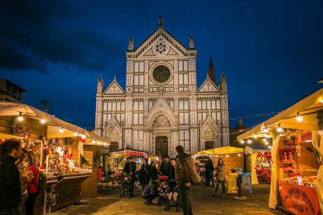 Twilight scene at Piazza Santa Croce in Florence, with the illuminated facade of the Basilica di Santa Croce and a vibrant street market filled with locals and tourists