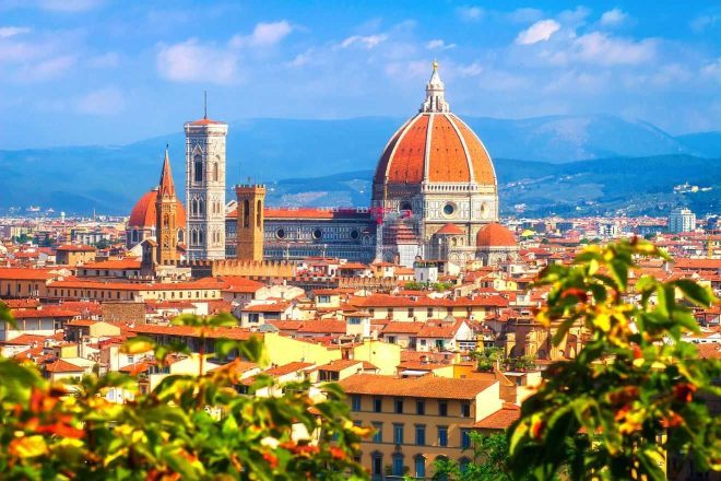 A vibrant view of Florence's iconic Cathedral of Santa Maria del Fiore, with its massive dome and bell tower, set against the backdrop of the city's historic buildings and distant rolling hills