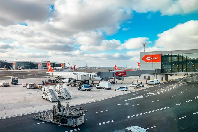 Istanbul Ataturk Airport with various airplanes on the tarmac, including Turkish Airlines jets, service vehicles, and the terminal buildings in the background