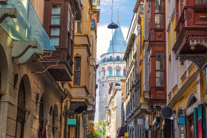 A narrow street in Istanbul with historic, multicolored buildings leading towards the iconic Galata Tower under a clear blue sky