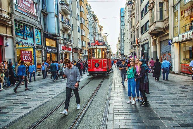 Busy Istiklal Street in Istanbul with people walking and a vintage red tram in the middle, surrounded by buildings with commercial signs