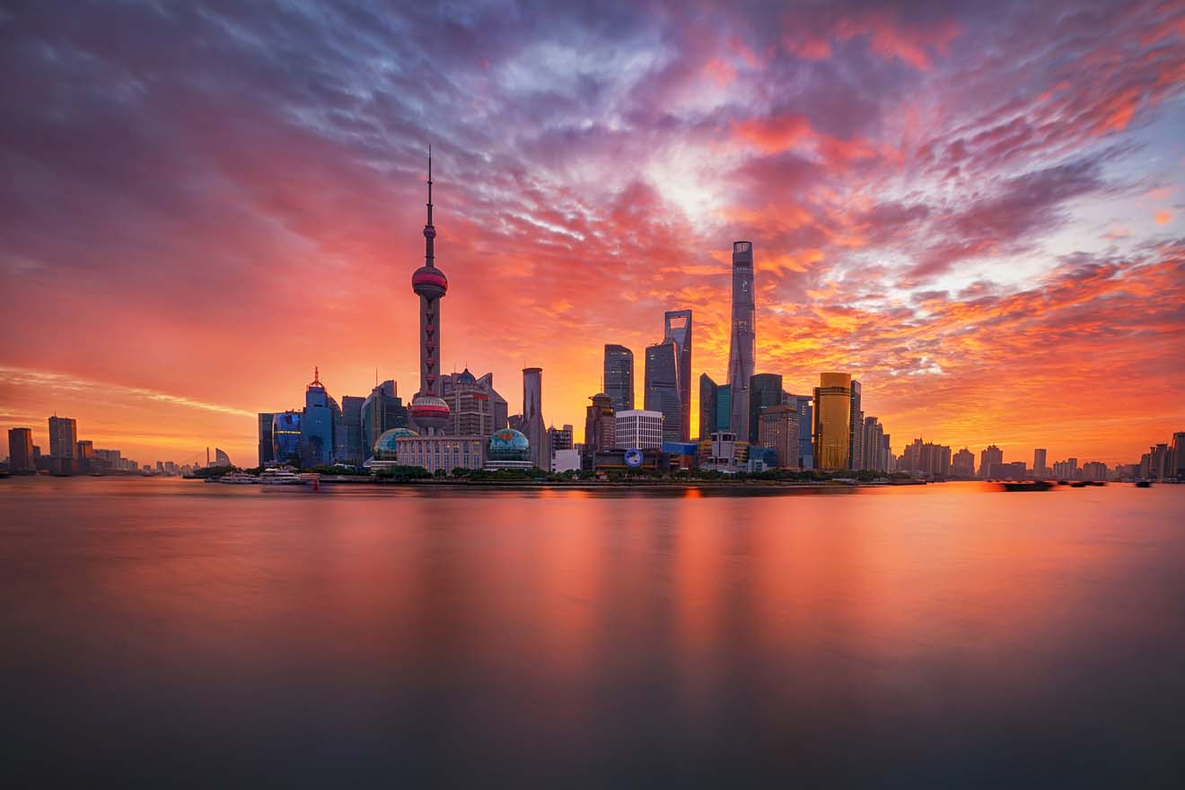 Sunset over the Shanghai skyline with the Oriental Pearl Tower and surrounding skyscrapers reflected in the Huangpu River under a fiery sky