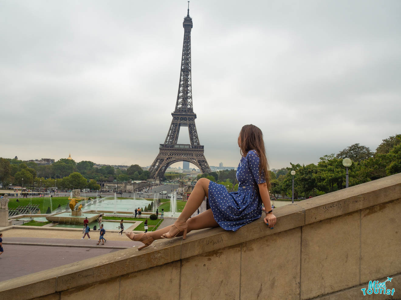 A woman sitting on a ledge in front of the eiffel tower.