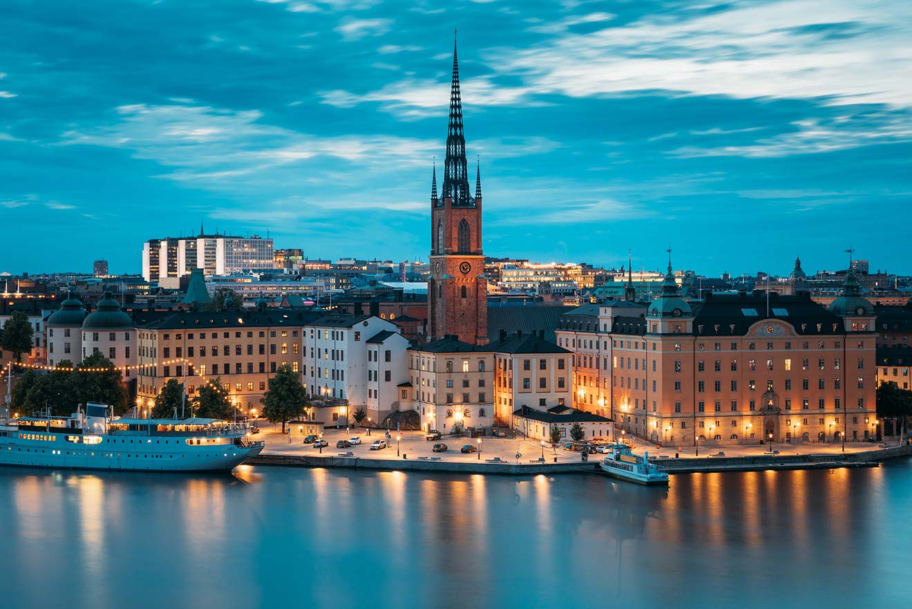 Evening view of Stockholm with Riddarholmen Church spire against a twilight sky and city lights reflecting in the water
