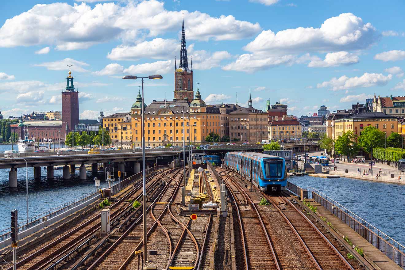 Train entering a station with Stockholm's old town and city hall in the background
