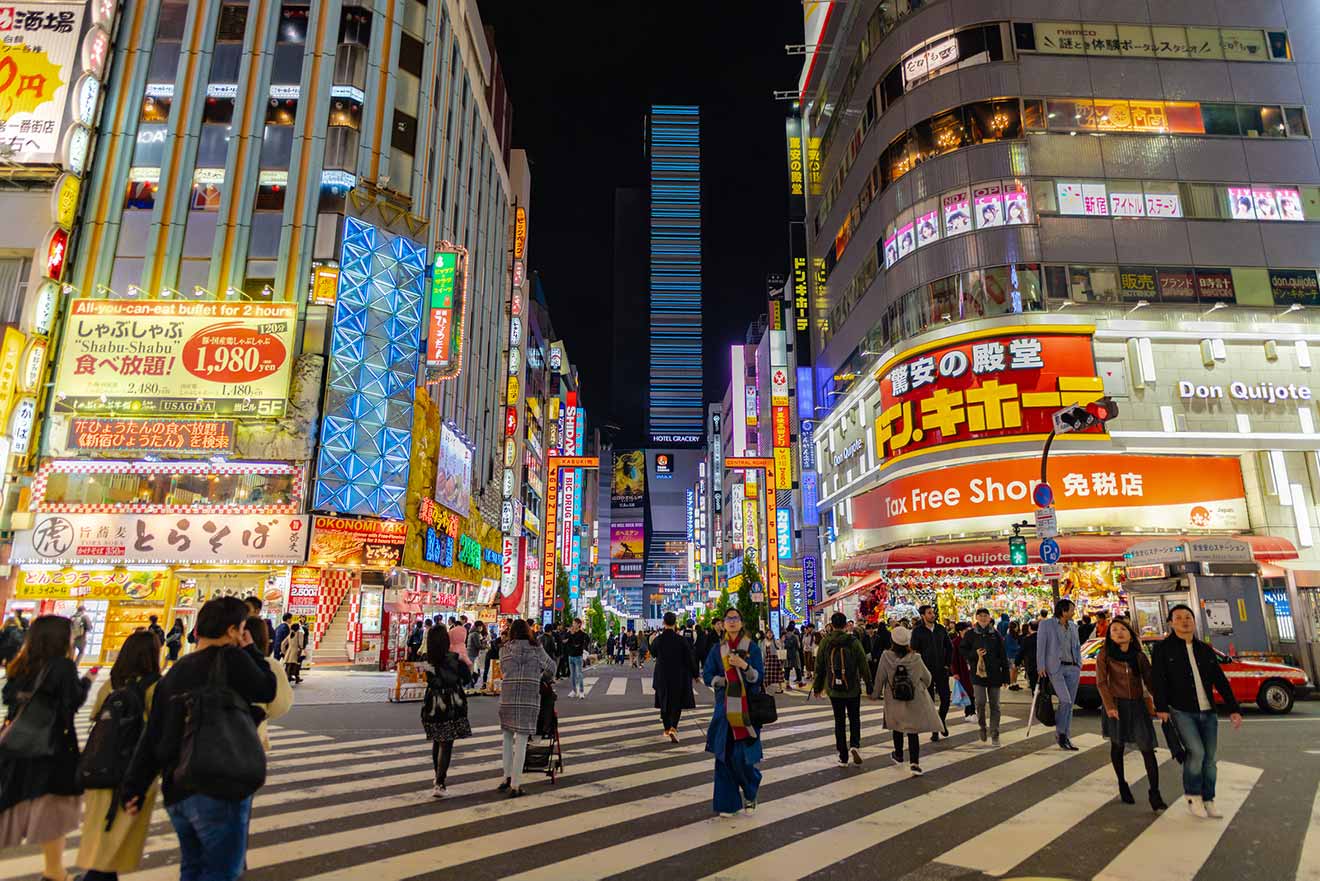 Bustling night scene at Shinjuku, Tokyo, with brightly lit billboards, and crowds on a pedestrian crossing