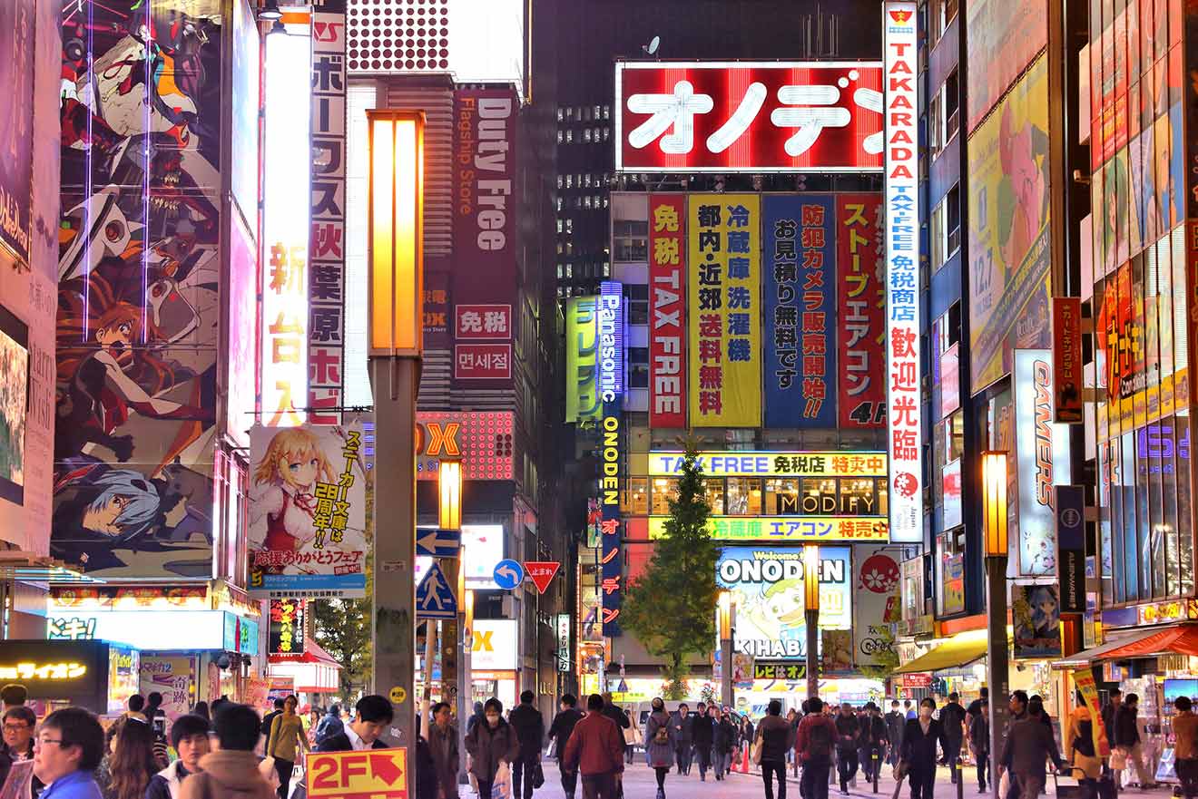 A lively pedestrian area in Akihabara, Tokyo, lit by the glow of anime and manga-related billboards and signs