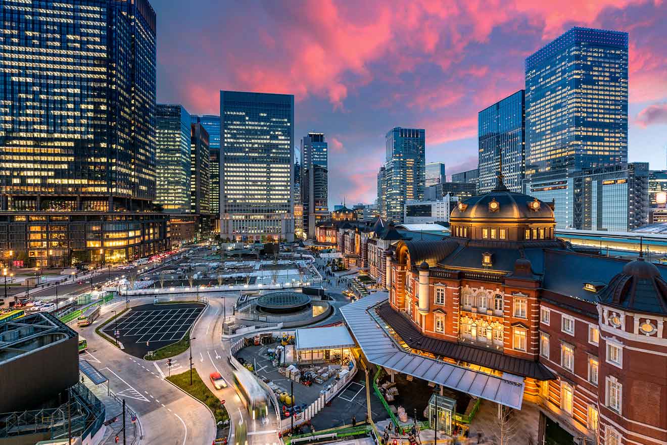 Tokyo Station and its surrounding modern skyscrapers at twilight, with the glow of the setting sun in the background