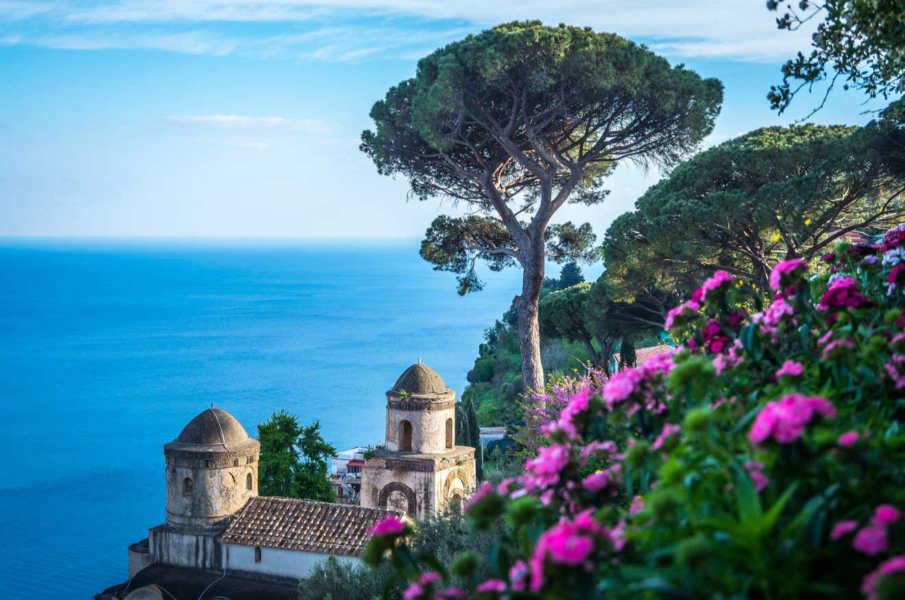 A view of the ocean with pink flowers and a church in the background in the city of Ravello on the Amalfi Coast, Italy