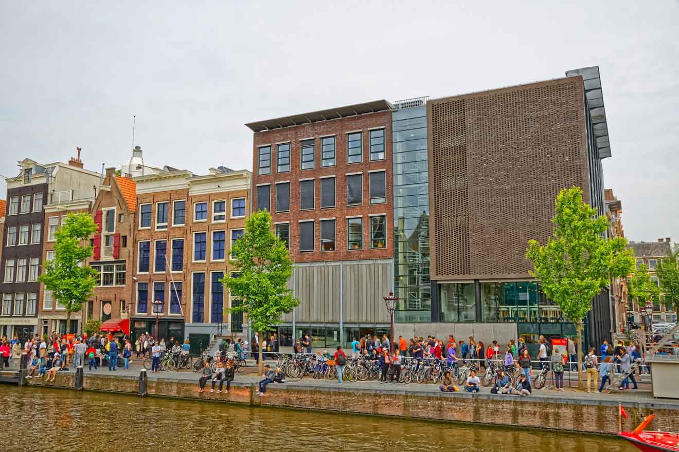 A vibrant canal-side scene in Amsterdam featuring a mix of traditional and modern architecture with people and bicycles lining the bustling sidewalk