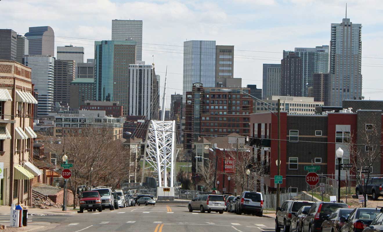 View of downtown Denver with various buildings and architectural styles, seen from a street with traffic signs indicating Boulder and Colfax avenues