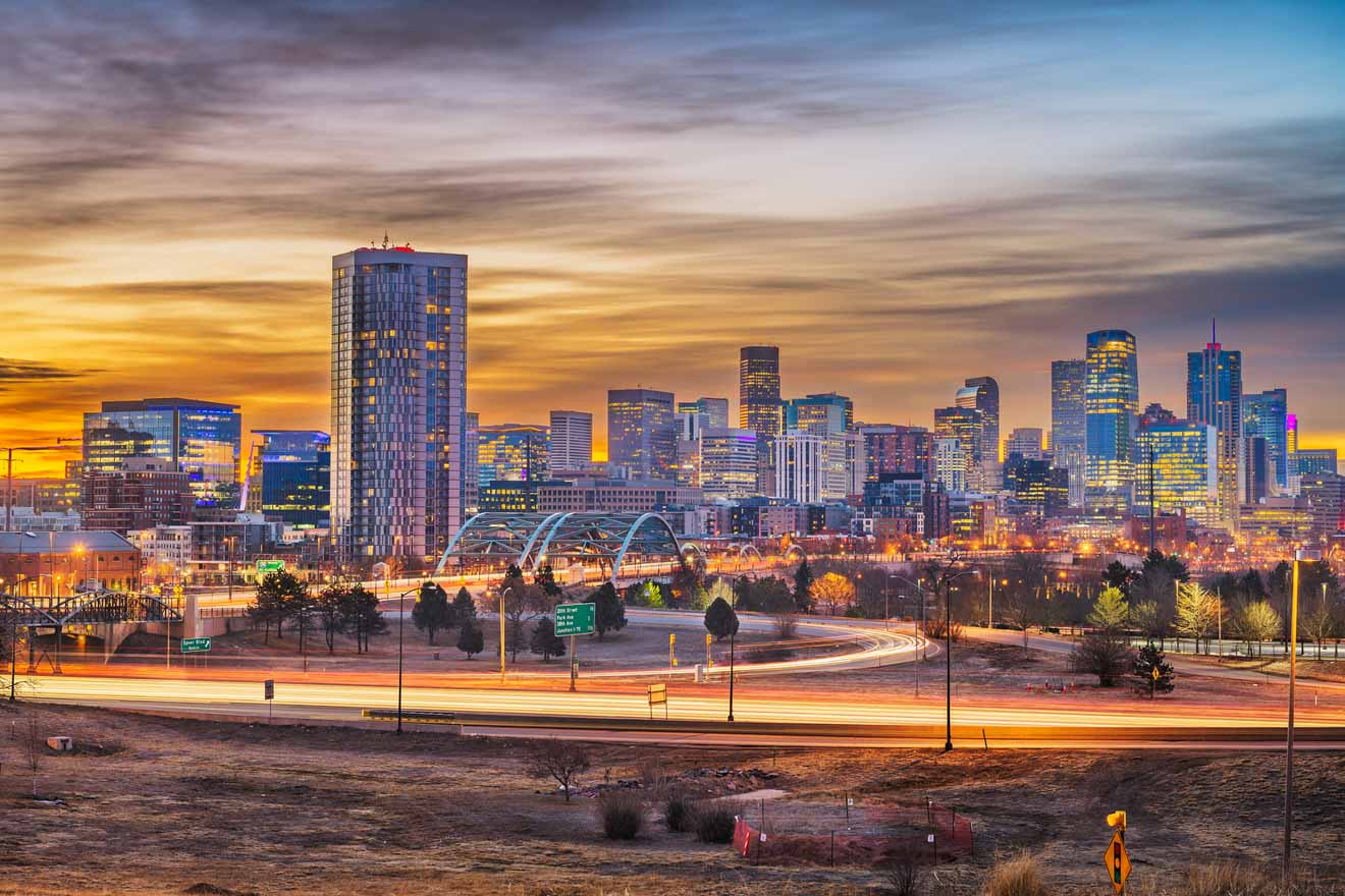 Sunrise over Denver, with the city skyline against a vibrant sky and streetlights trailing along the highway, emphasizing the early morning hustle