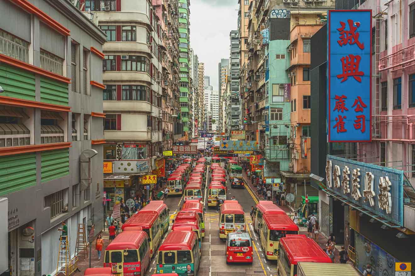 A busy Hong Kong street lined with tall buildings, featuring numerous red minibuses and a crowd of people, capturing the city's dynamic public transportation system.