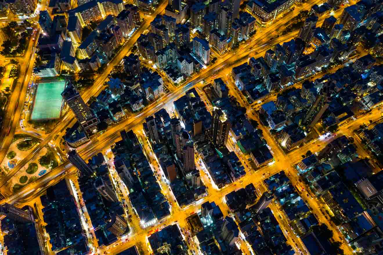 An aerial nighttime view of Hong Kong, displaying the city's dense layout with streets and buildings illuminated in a grid-like pattern.