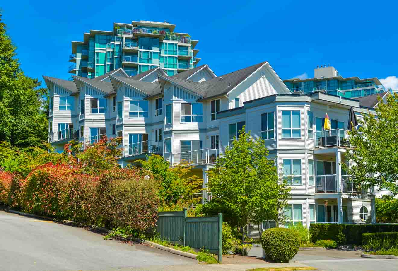 Residential neighborhood in Vancouver with multi-story houses surrounded by lush greenery under a clear blue sky.