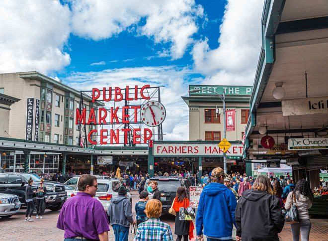 Busy scene at Seattle's iconic Pike Place Market with the 'Public Market Center' neon sign overhead and people milling about