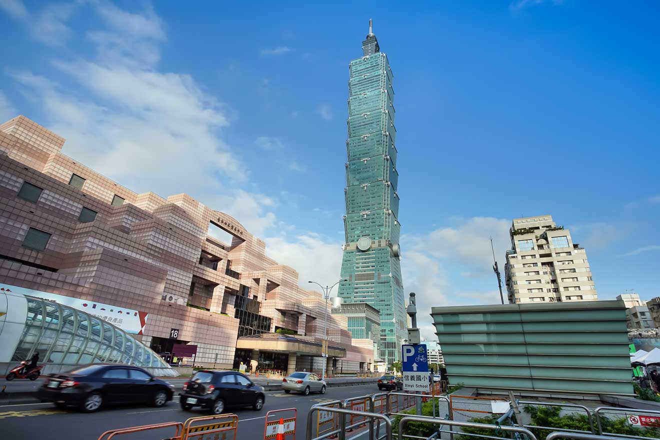 Taipei 101 seen from street level with surrounding modern architecture under a blue sky.