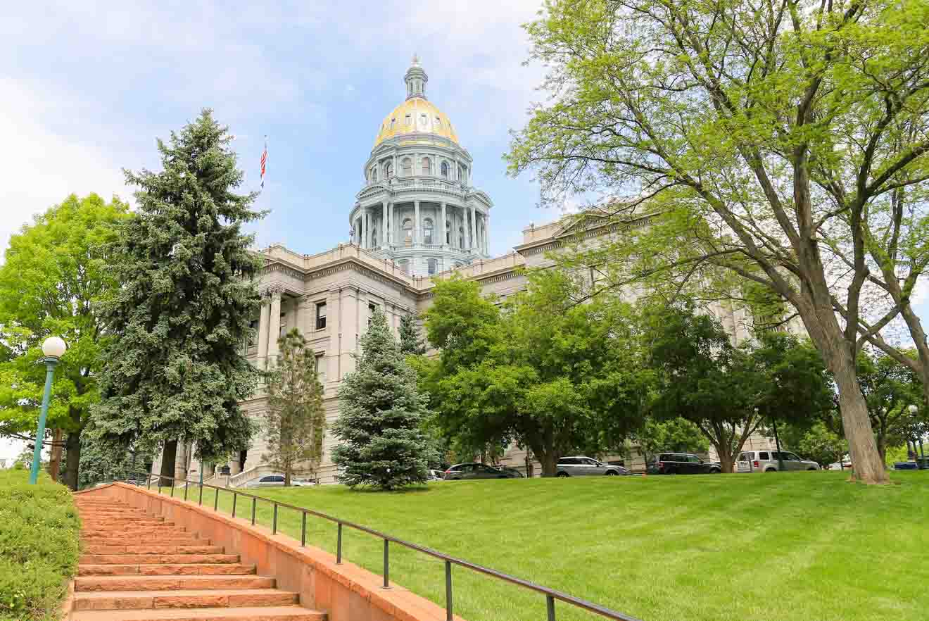 The majestic Colorado State Capitol building with its golden dome, surrounded by green trees and a well-kept lawn, symbolizing government and architecture