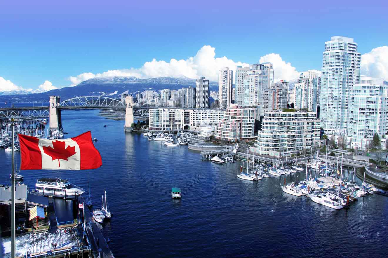 Sunny day in Vancouver with a Canadian flag in the foreground and the city skyline across the harbor.