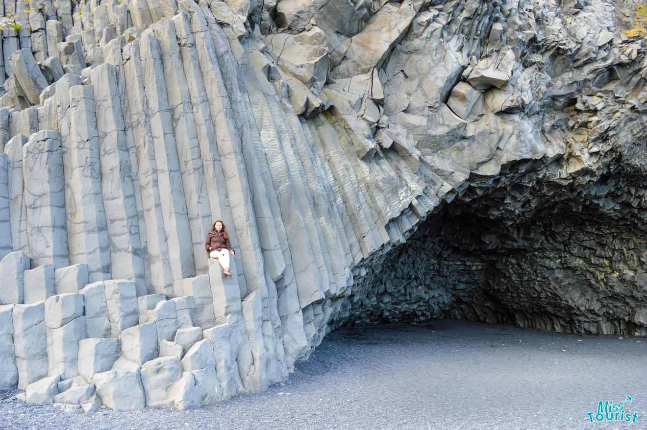 The woman sits on the rocks on the black sand beach island