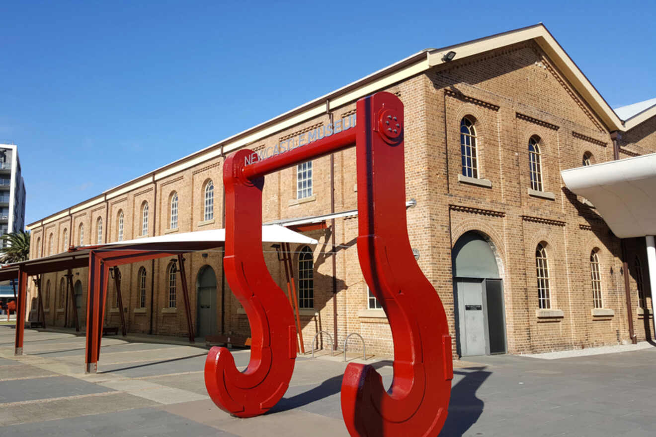 A historic brick building with large red metal hooks outside under a blue sky.