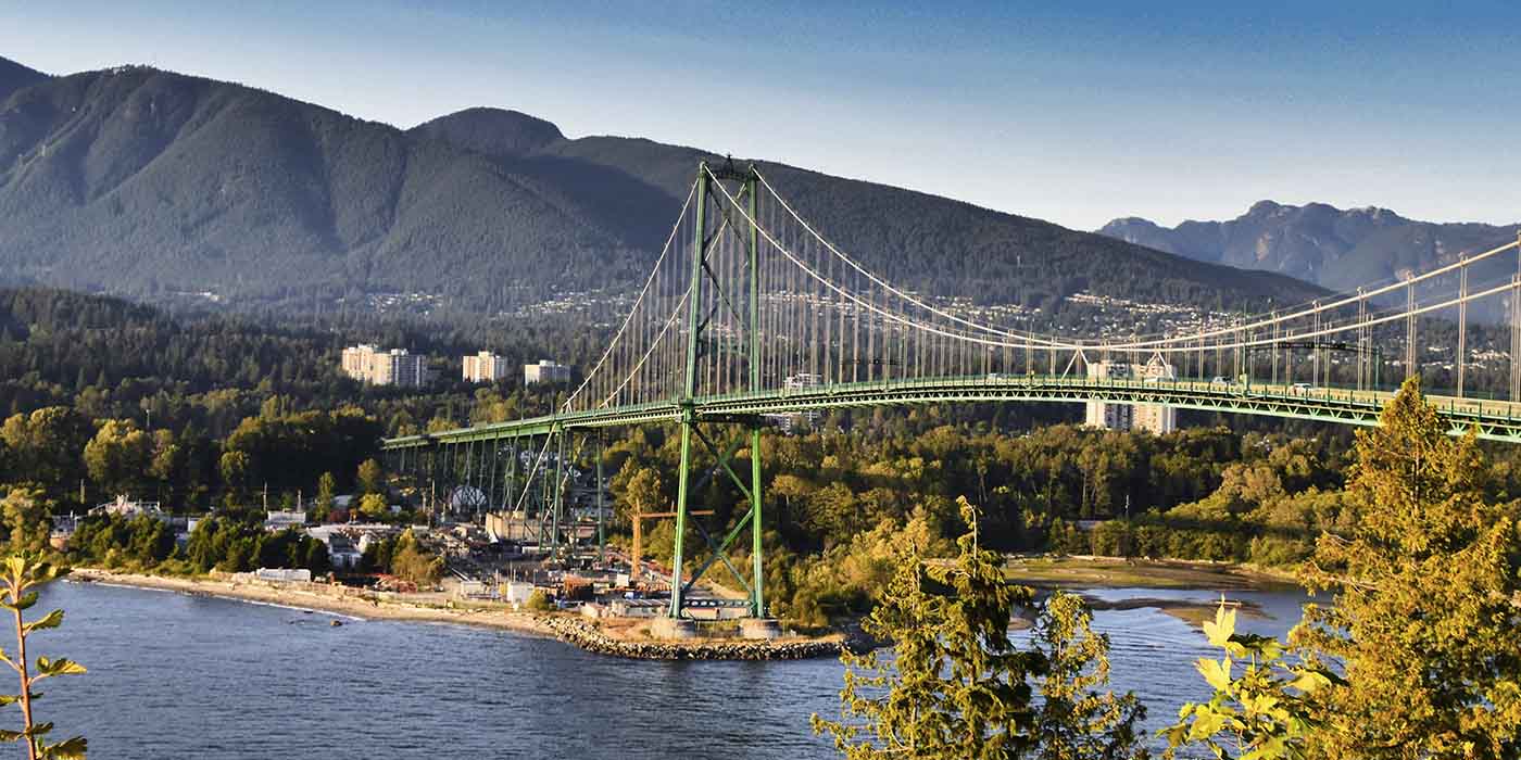 Lions Gate Bridge in Vancouver during the daytime, with lush greenery and mountains in the background.