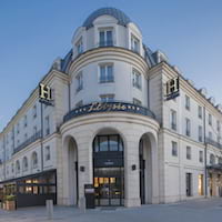 Exterior view of a large, modern hotel building with multiple stories, arched windows, a dome roof, and "Hotel" signage on the facade.