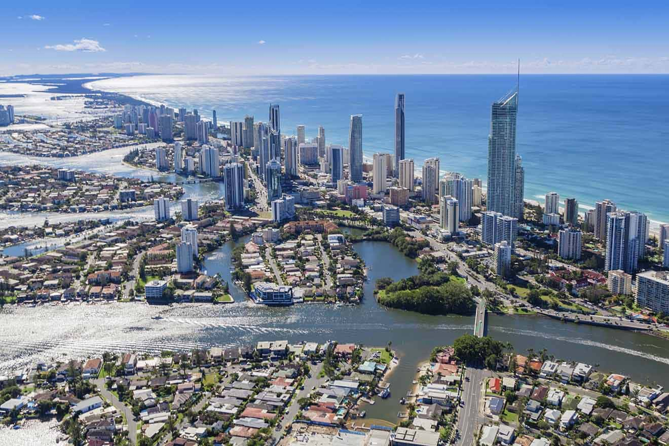 Aerial view of a coastal city with tall skyscrapers, winding waterways, and residential areas, bordered by a blue ocean.