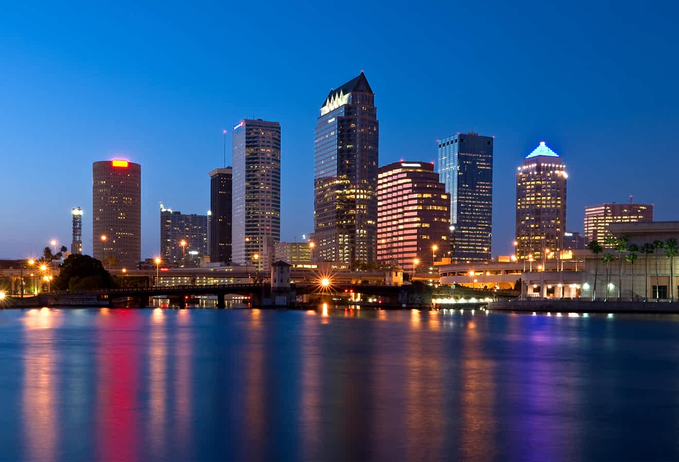 Twilight skyline of Tampa with illuminated buildings reflected in the water.