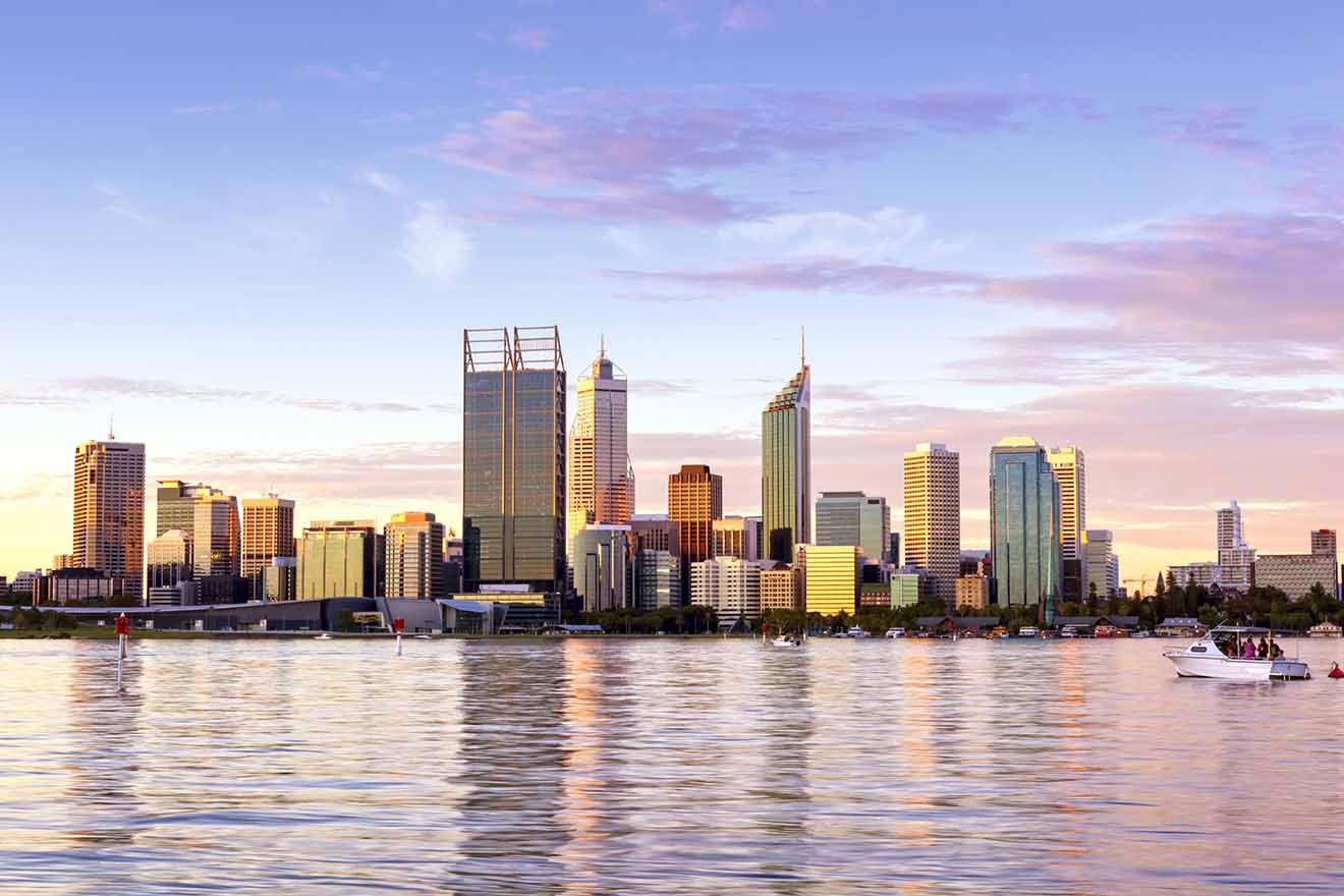 A tranquil evening view of a city skyline reflected in the water, with pastel skies above and a small boat on the river