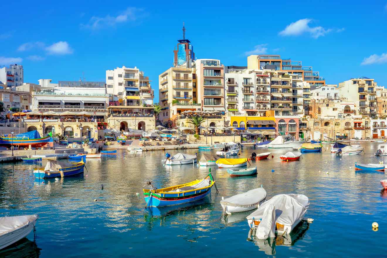 Colorful boats in a calm harbor with modern and traditional buildings in the background under a clear blue sky.