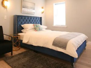 Minimalist bedroom with a stately blue upholstered bed, small side table, and wall-mounted lamps