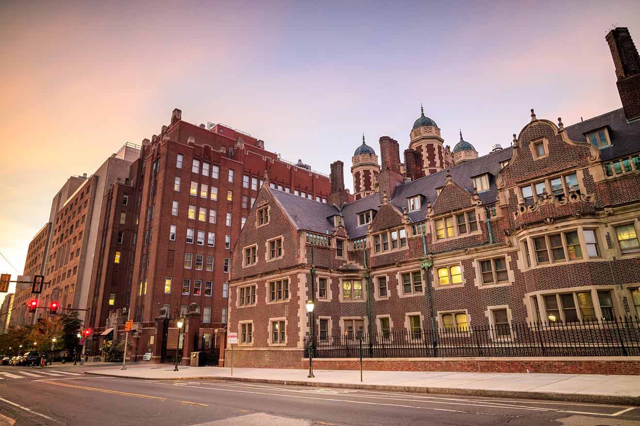 The sun setting behind a historical, multi-architectural style building on an urban street, casting a warm glow on the ornate brick façade