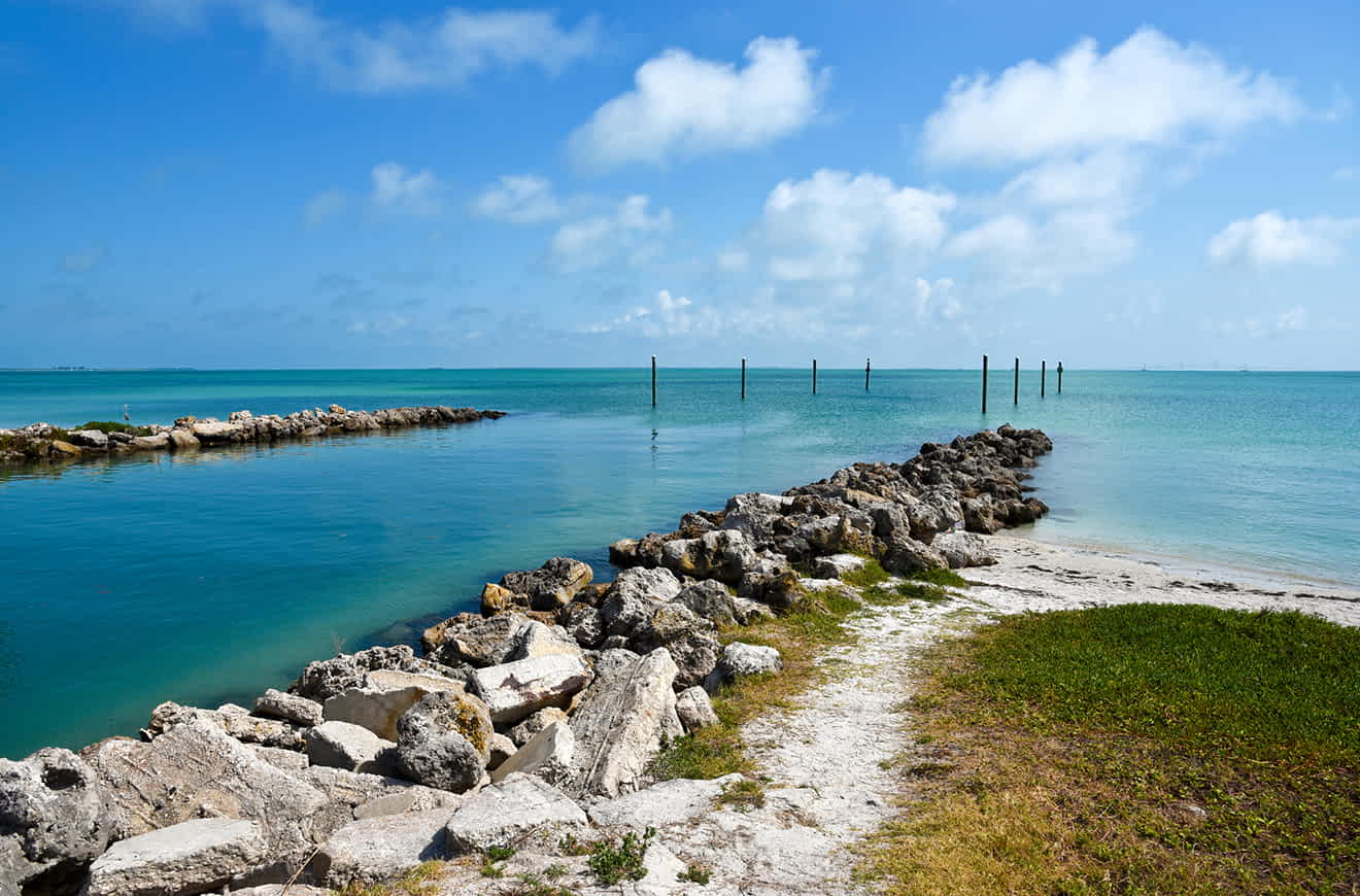 Serene coastal scene with a rocky shoreline leading to calm blue waters under a clear sky