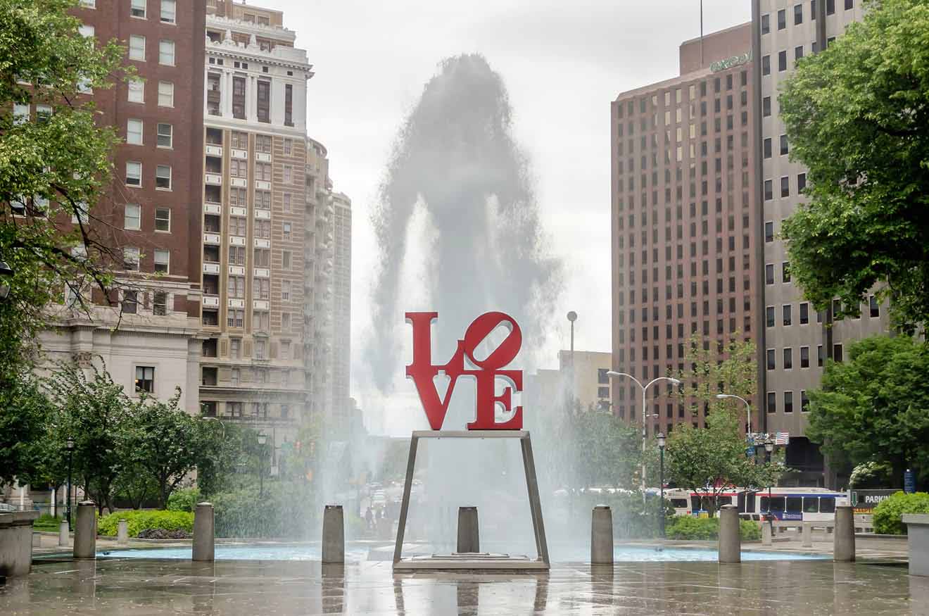 The iconic red LOVE sculpture in Philadelphia’s LOVE Park with a fountain mist backdrop and surrounding urban architecture