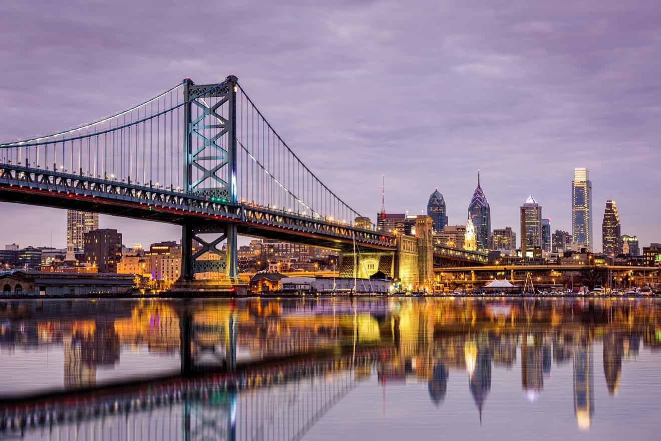 The Benjamin Franklin Bridge in Philadelphia during twilight, with its suspension cables illuminated above the calm waters reflecting city lights