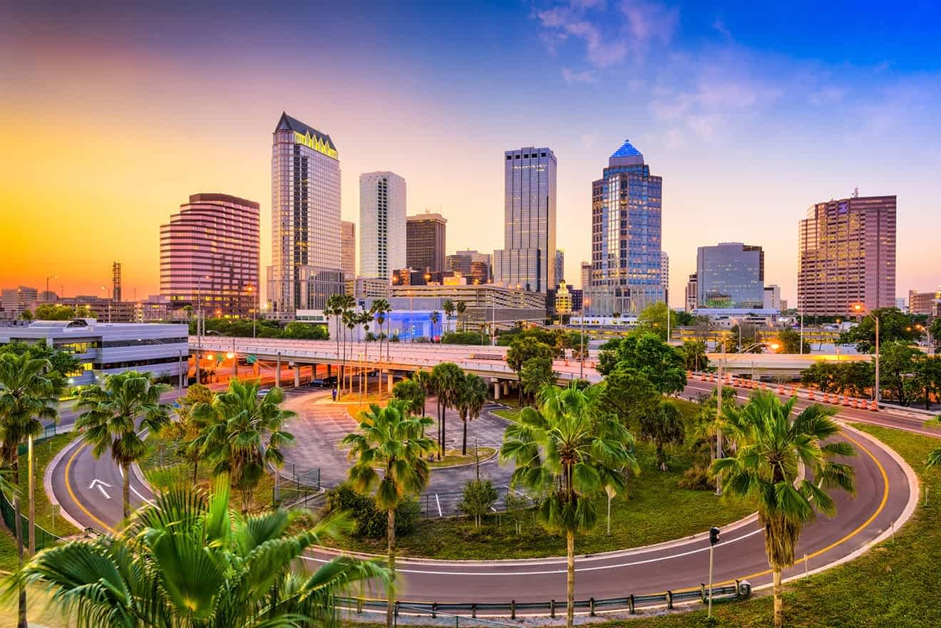 Dusk skyline of Tampa with the sun setting behind skyscrapers and palm trees in the foreground