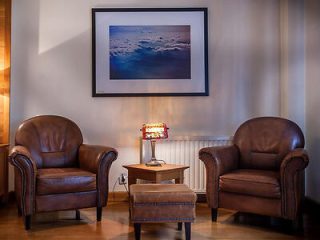 A reading nook with two classic leather armchairs, a vintage lamp, and framed artwork on the wall