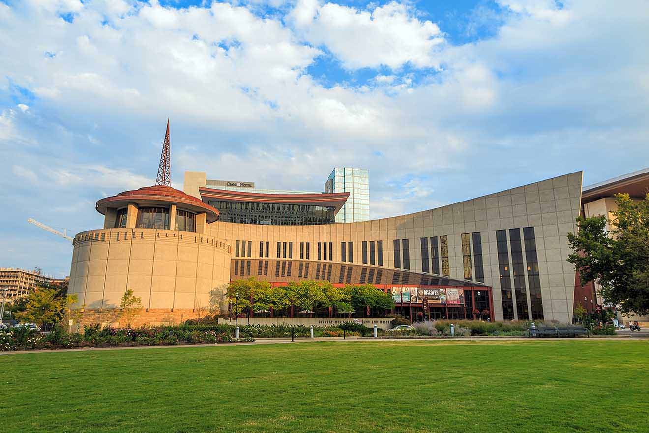 The Country Music Hall of Fame building in Nashville, set against a clear sky with surrounding greenery and urban development in the background