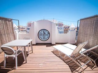 A private rooftop terrace with wooden flooring and a white round table with chairs, surrounded by high walls for privacy
