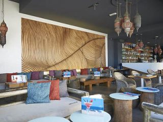 A stylish hotel lobby interior with wooden wall decor creating wave patterns, eclectic furniture with colorful cushions, and ornate lanterns