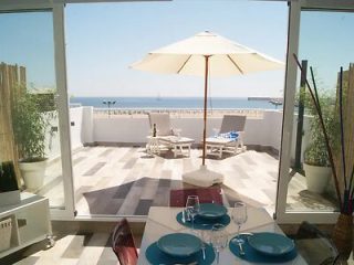 A bright and airy beachfront dining area with large glass doors open to a terrace with an umbrella and lounge chairs overlooking the sea