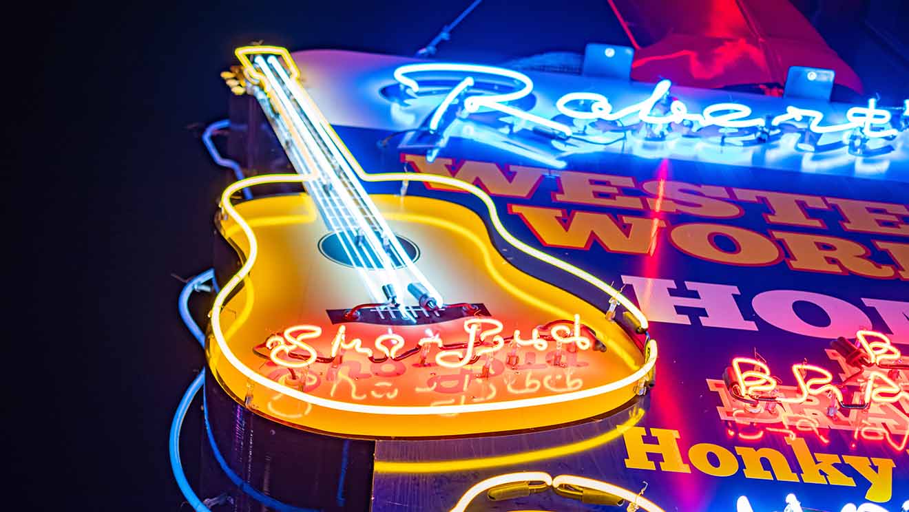Vibrant neon sign of Robert's Western World, a famous honky-tonk bar in Nashville, featuring a guitar and bright lights against a night sky.