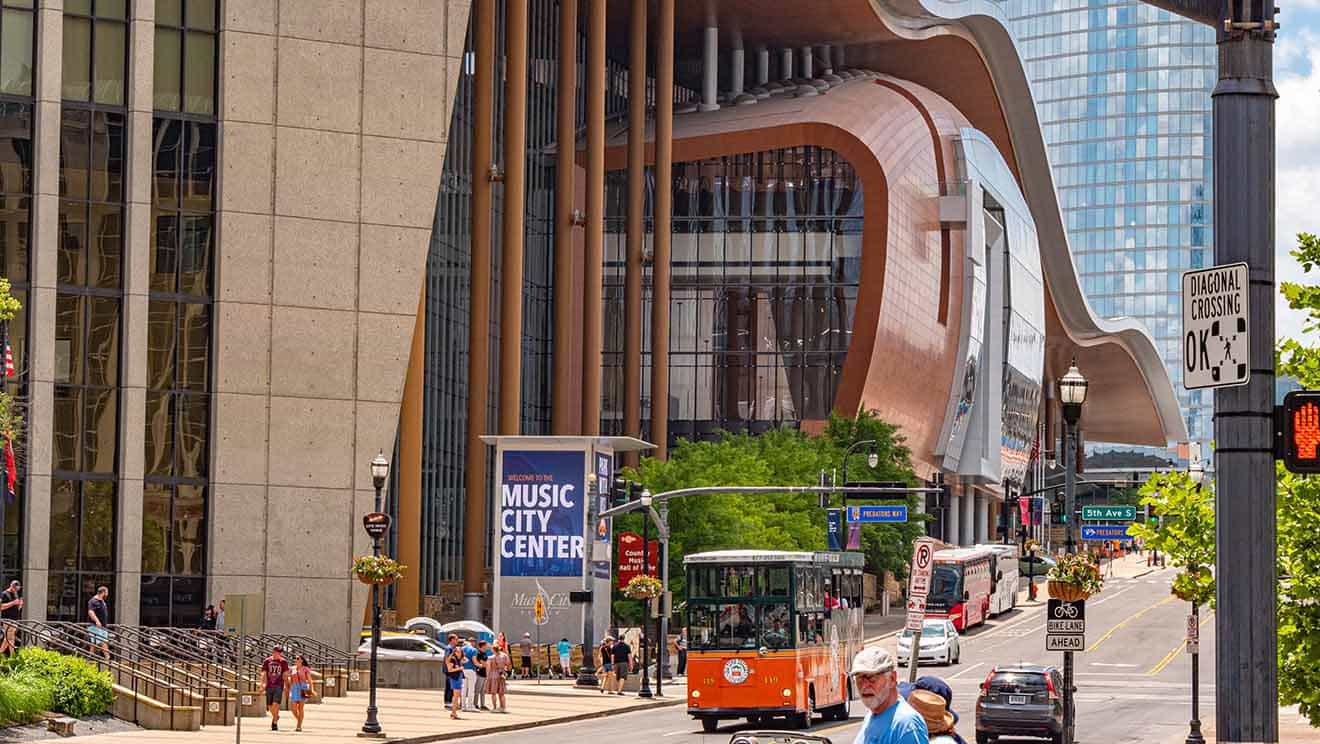 Bustling street view with the Music City Center's modern architecture on a sunny day in Nashville, featuring pedestrians and a red trolley bus