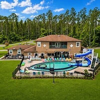 Two-story house with a fenced backyard featuring a large swimming pool, water slide, lounge chairs, and surrounded by grass and trees.