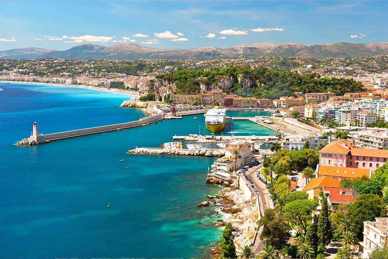 Aerial view of a Nice, France with clear blue waters, a large cruise ship docked at a pier, and a mountainous backdrop, showcasing the vibrant urban landscape by the sea.