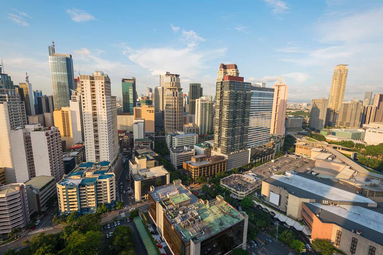 Aerial view of Makati, the financial district of Manila, Philippines, showcasing modern skyscrapers, bustling streets, and green spaces in the late afternoon sun.