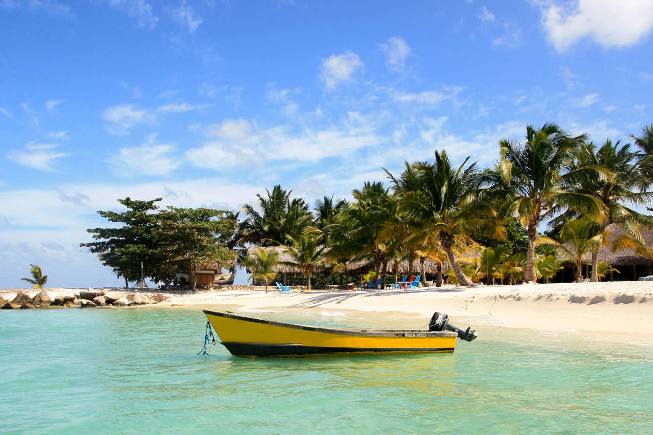 Serene tropical beach scene in Punta Cana with a yellow boat moored in crystal-clear turquoise water, surrounded by palm trees and a clear blue sky.