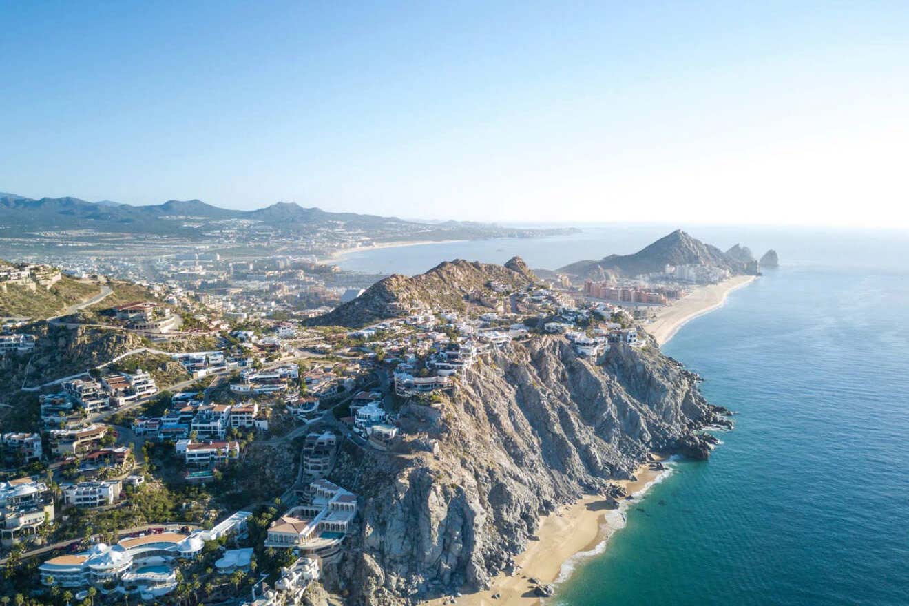 Aerial view of a coastal town with houses dotting the rugged landscape and clear blue waters.
